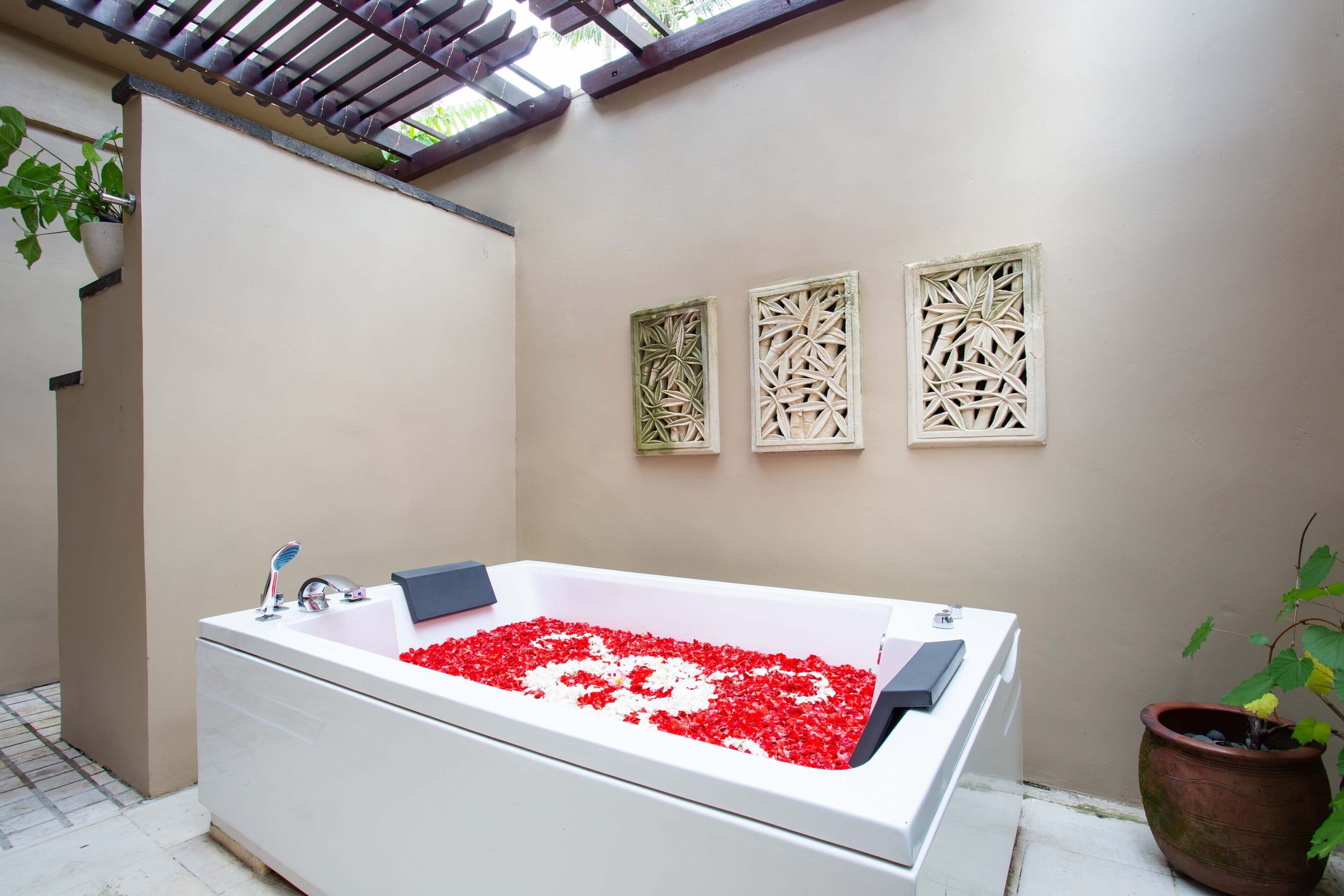 A modern bathroom with a large bathtub filled with red flowers, a potted plant, and decorative wall panels.