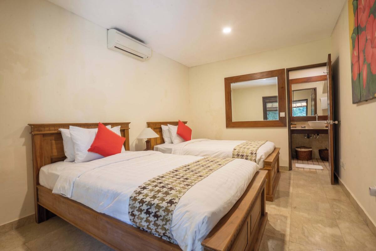 A hotel room with two wooden beds, white bedding, and a bathroom with a mirror and sink.