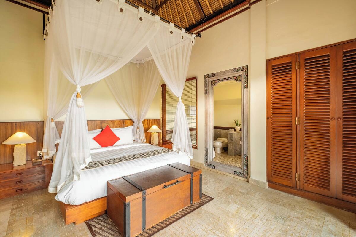 A bedroom with a four-poster bed, wooden bedside tables, a nightstand, a wooden bench, and a large mirror.