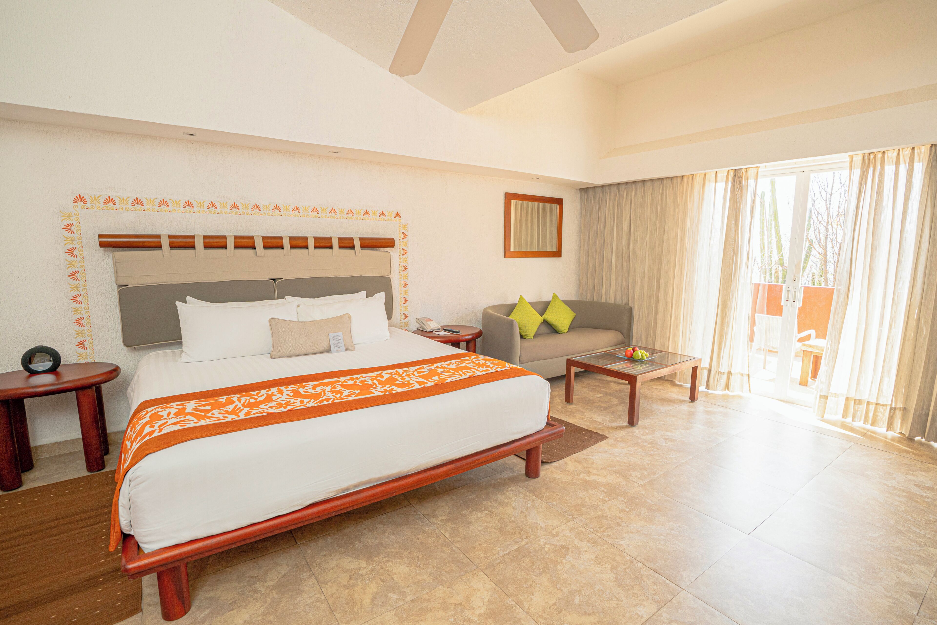 Una habitación de hotel con una cama grande, un sofá, una mesita y una ventana con cortinas.