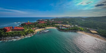 Vista aérea de un complejo turístico en la costa con varias construcciones, una playa y una vista despejada del océano.