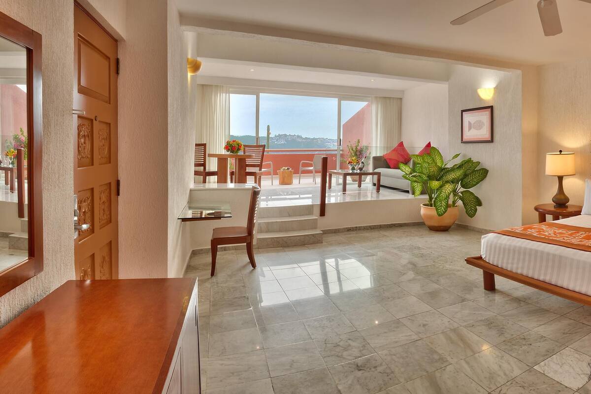 A hotel room with a large bed, two bedside tables, a ceiling fan, and a view of the outdoors.