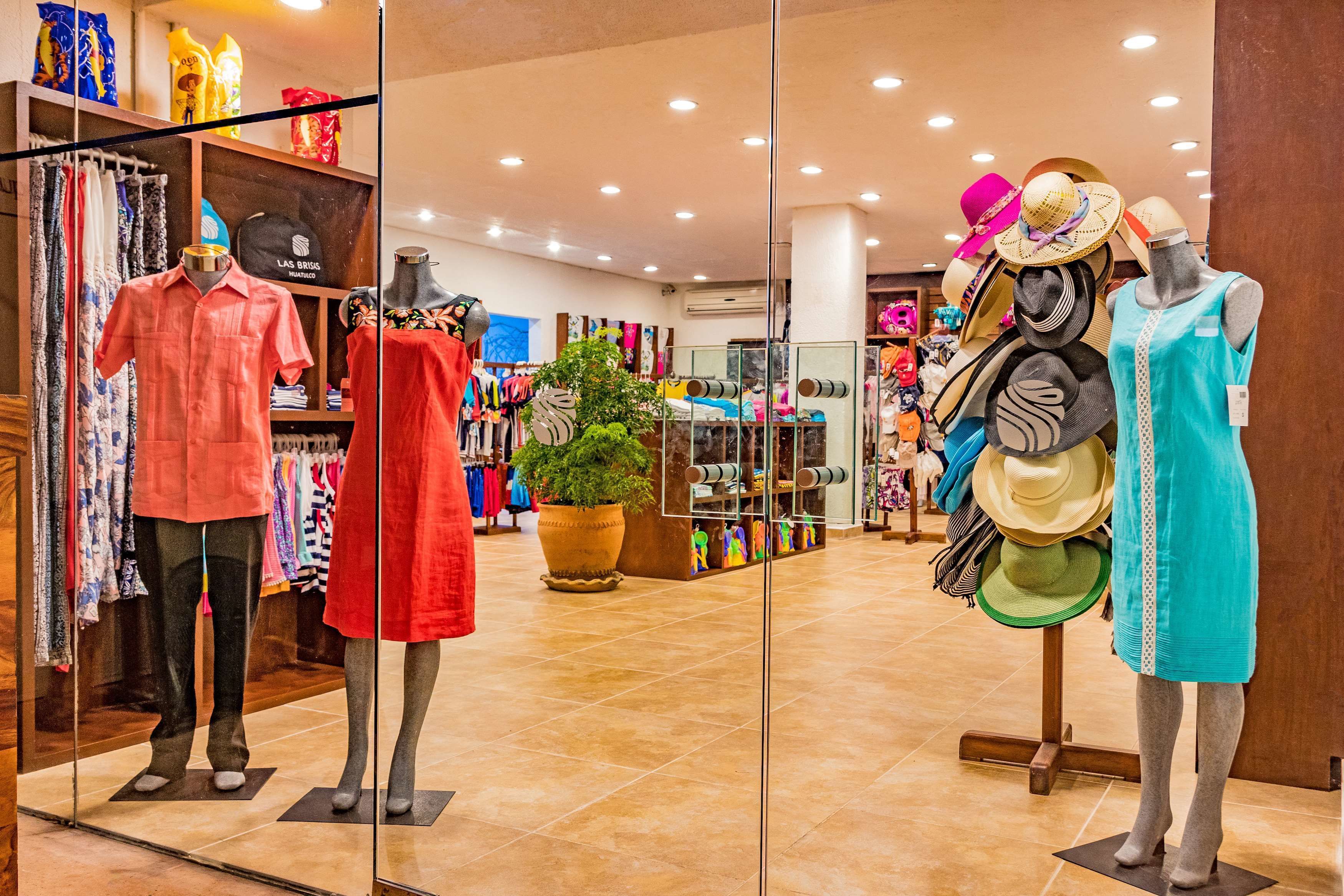 Una tienda de ropa con maniquíes mostrando diversos conjuntos, incluyendo un vestido rojo y un vestido turquesa.
