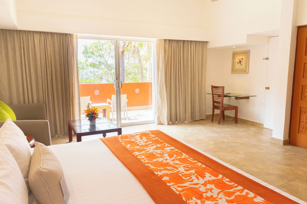 A hotel room with a bed, a desk, a chair, and a view through a glass door.