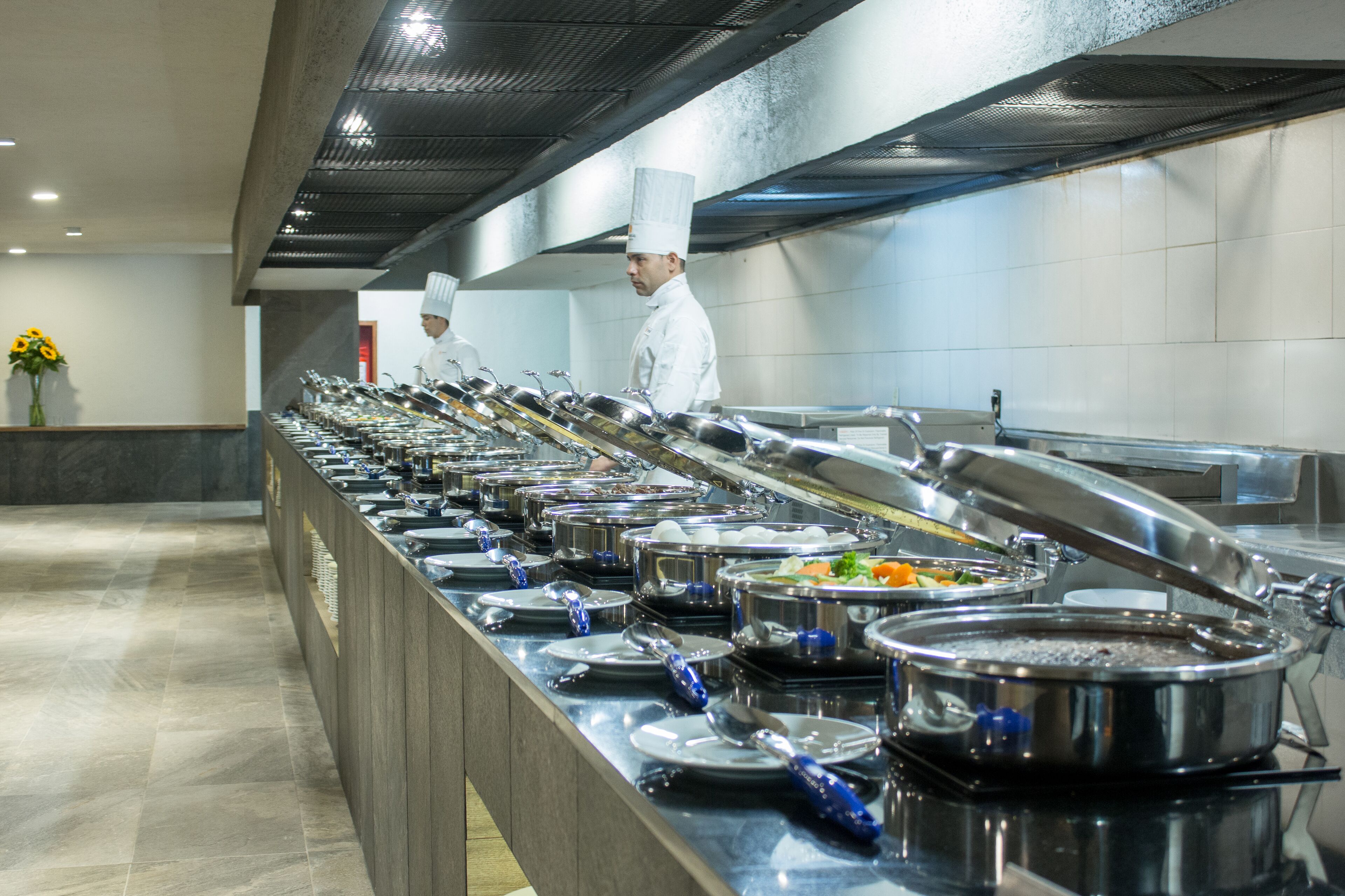 A buffet setup with multiple serving stations, a chef in uniform, and a tiled wall in the background.