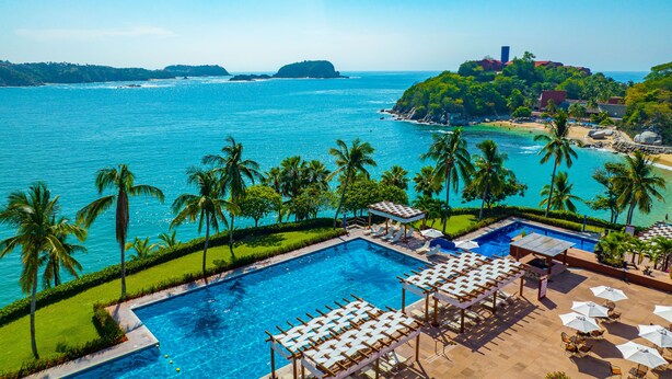 Zona de piscina en un resort, con vista al mar, palmeras y una isla distante.