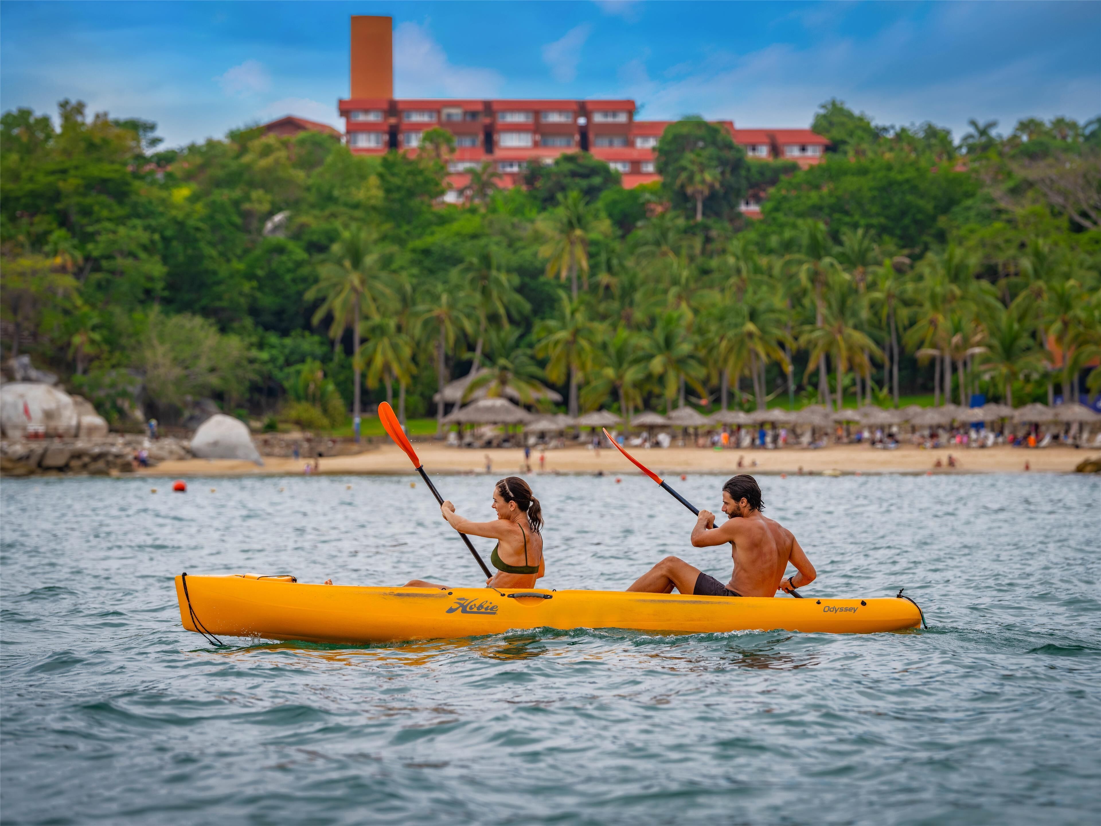 A yellow kayak on calm water with a beach and palm trees in the background.