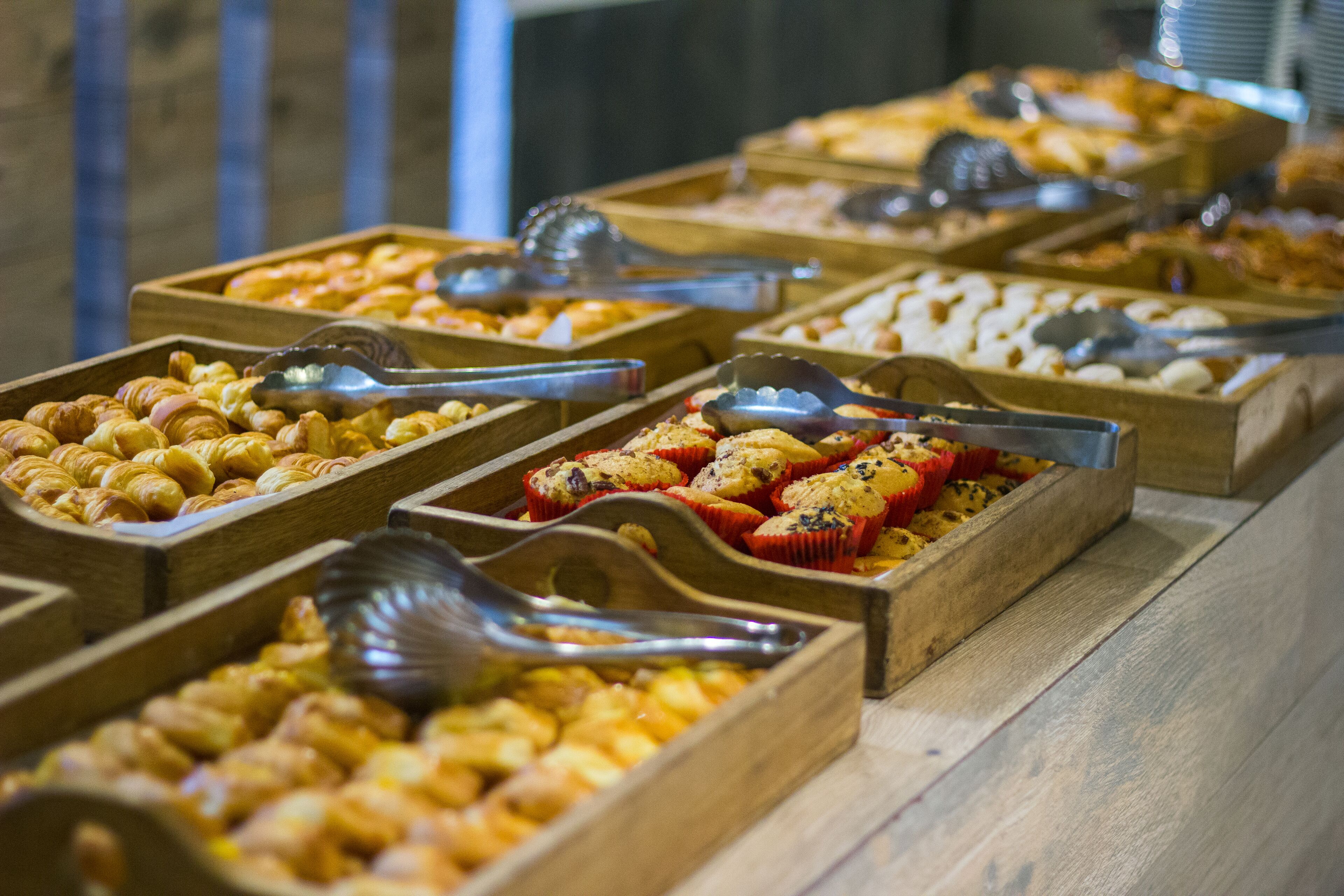 A buffet with various food items in wooden trays, each with serving utensils.