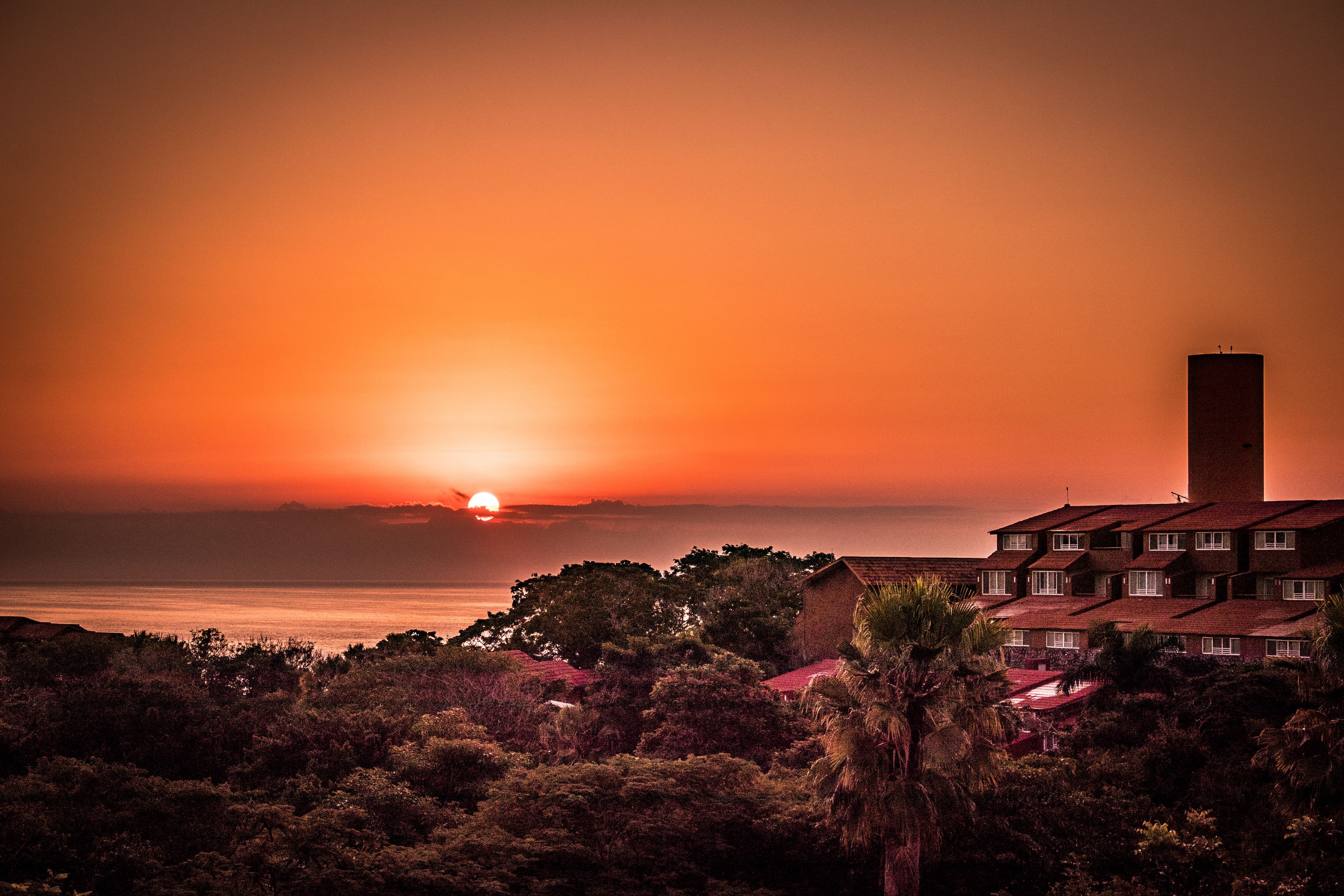 A coastal sunset view with a prominent tower and a multi-story building with balconies.