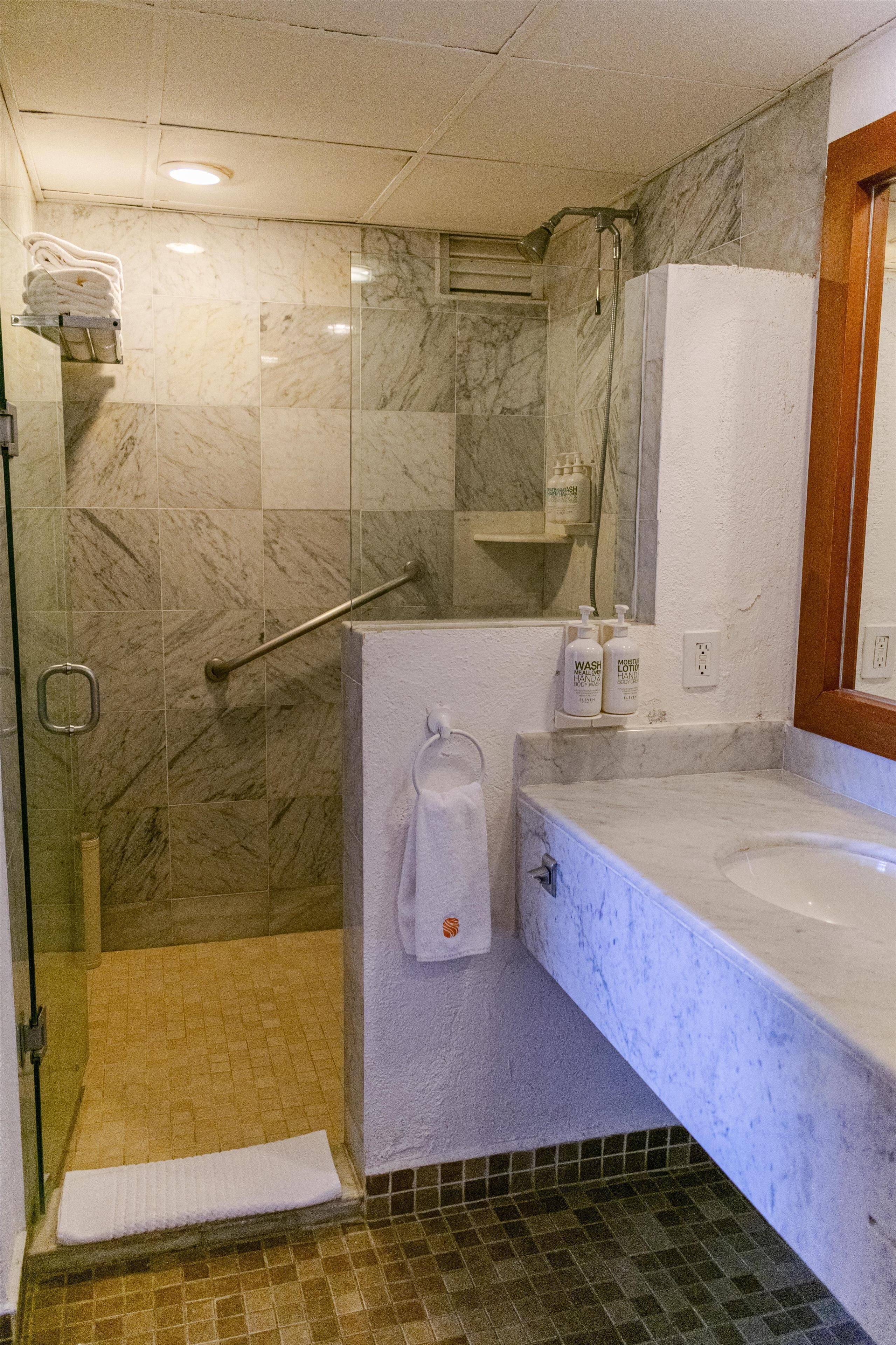 Un baño con cabina de ducha de vidrio, un lavamanos blanco y un espejo.