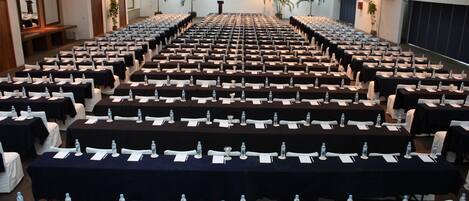 A conference room with rows of tables, each equipped with water bottles and notepads.