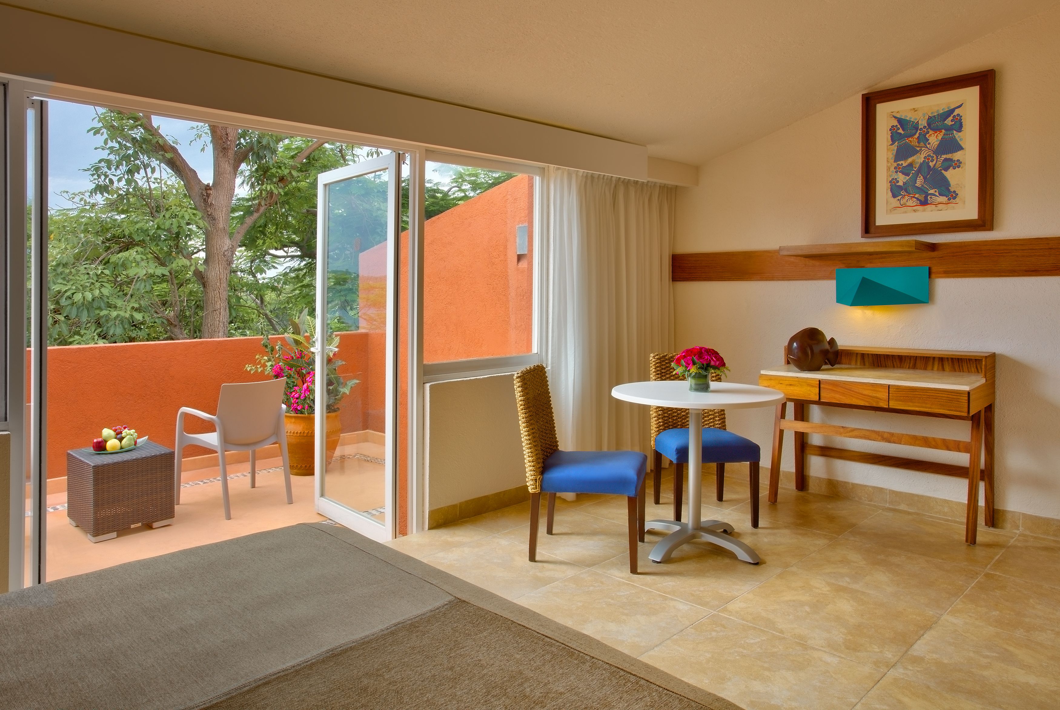 Una habitación con una mesa de comedor, sillas, un pequeño sofá, una mesita auxiliar y un ventanal con vistas a árboles y edificios.