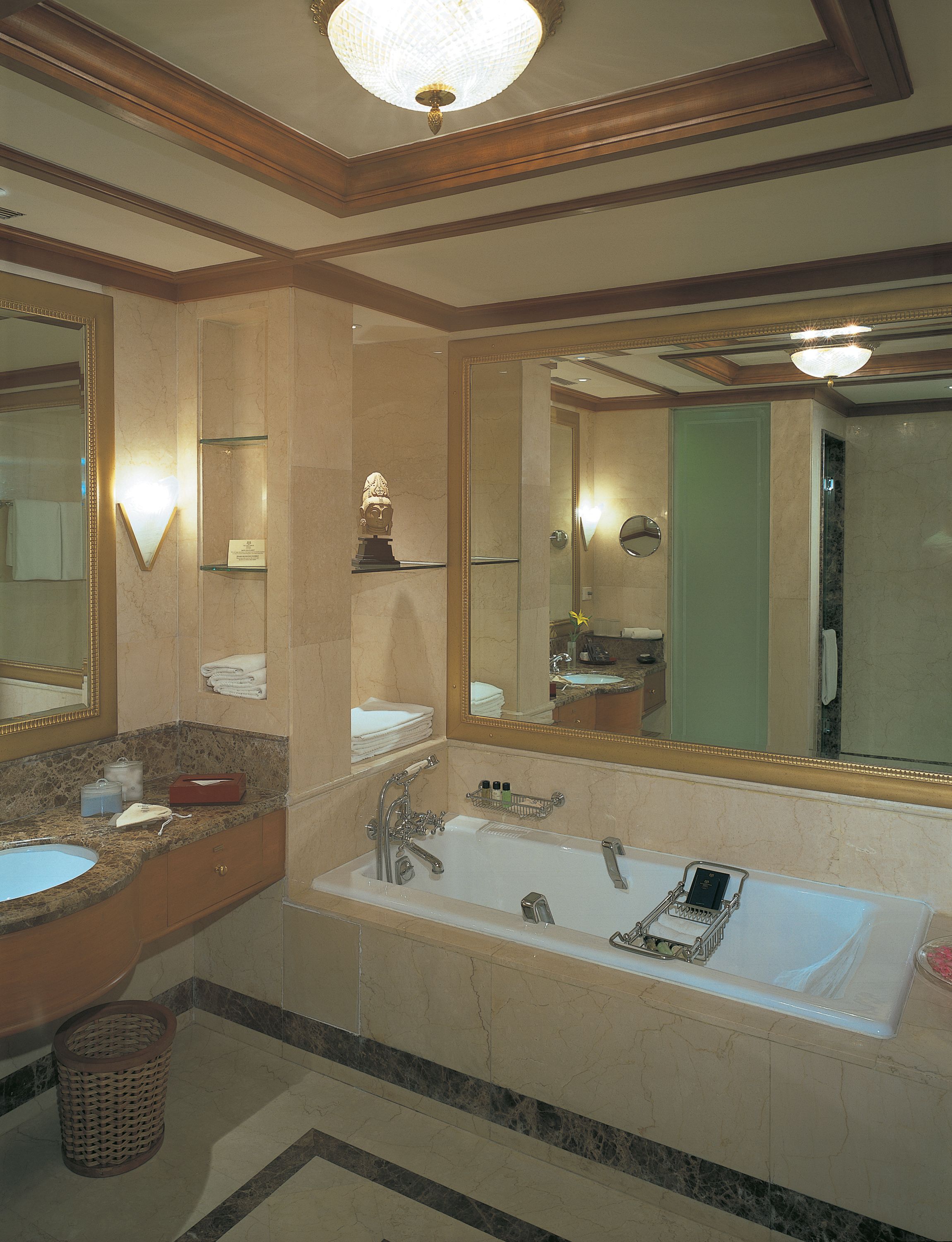 A bathroom with a large mirror, two sinks, a bathtub, and a vanity with a marble countertop.