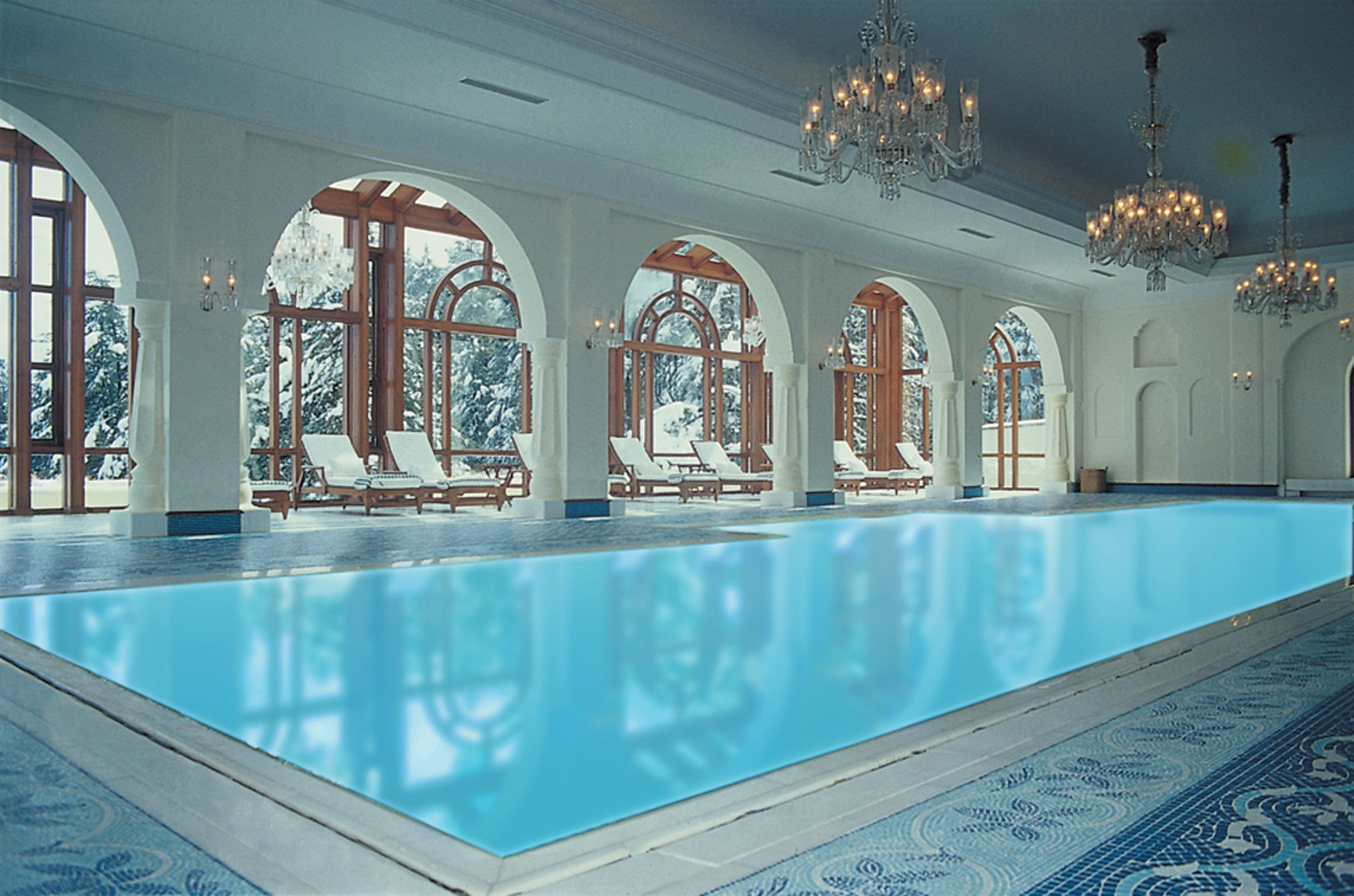 A large indoor swimming pool with arched windows and lounge chairs.