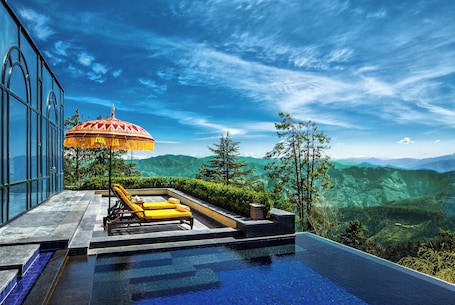 An infinity pool with a view of mountains, a red umbrella, and yellow lounge chairs.