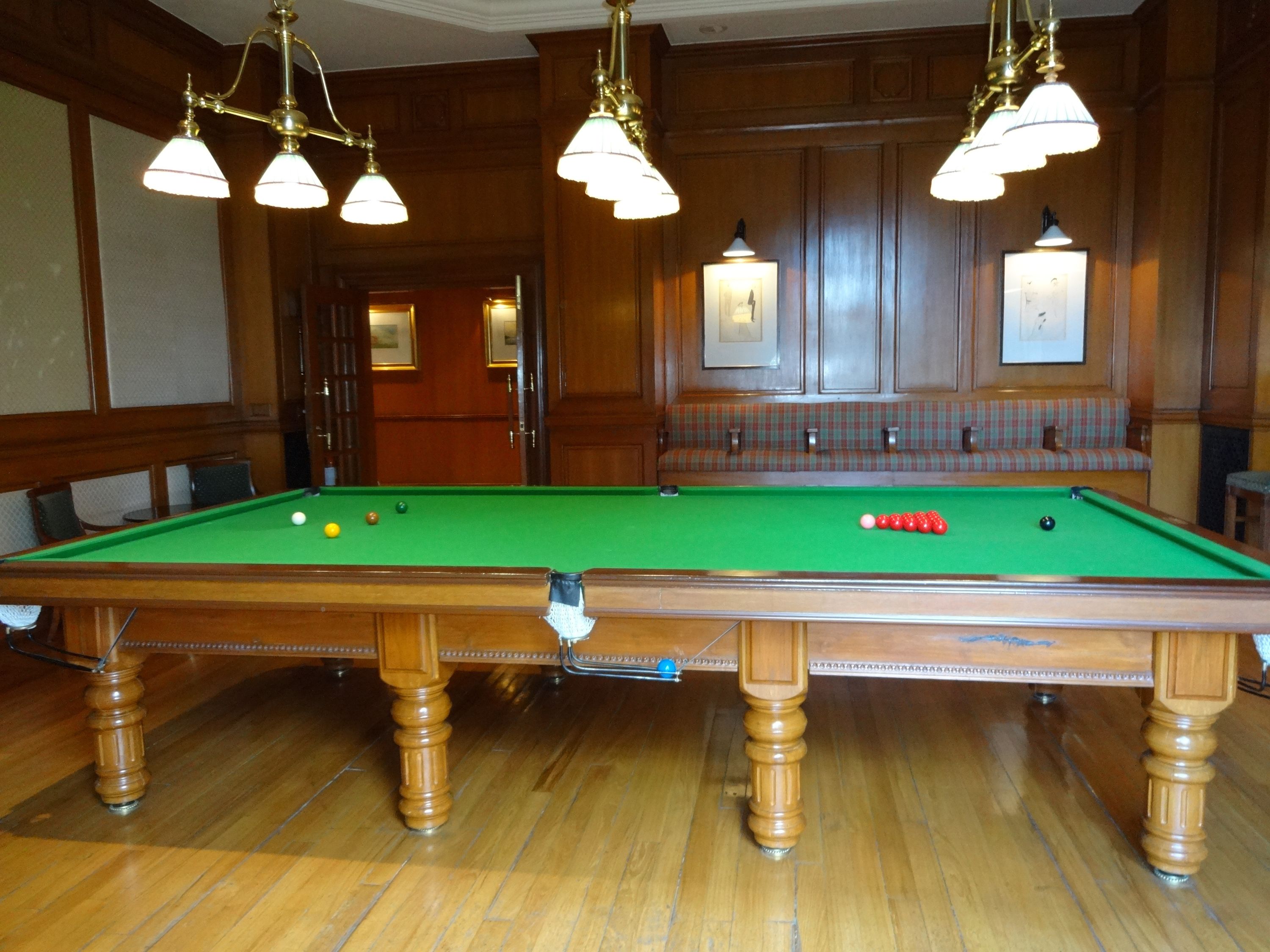 Une table de billard avec des billes, un plancher en bois et des lampes suspendues.