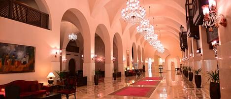 A spacious lobby with high ceilings, chandeliers, and a red carpeted floor.