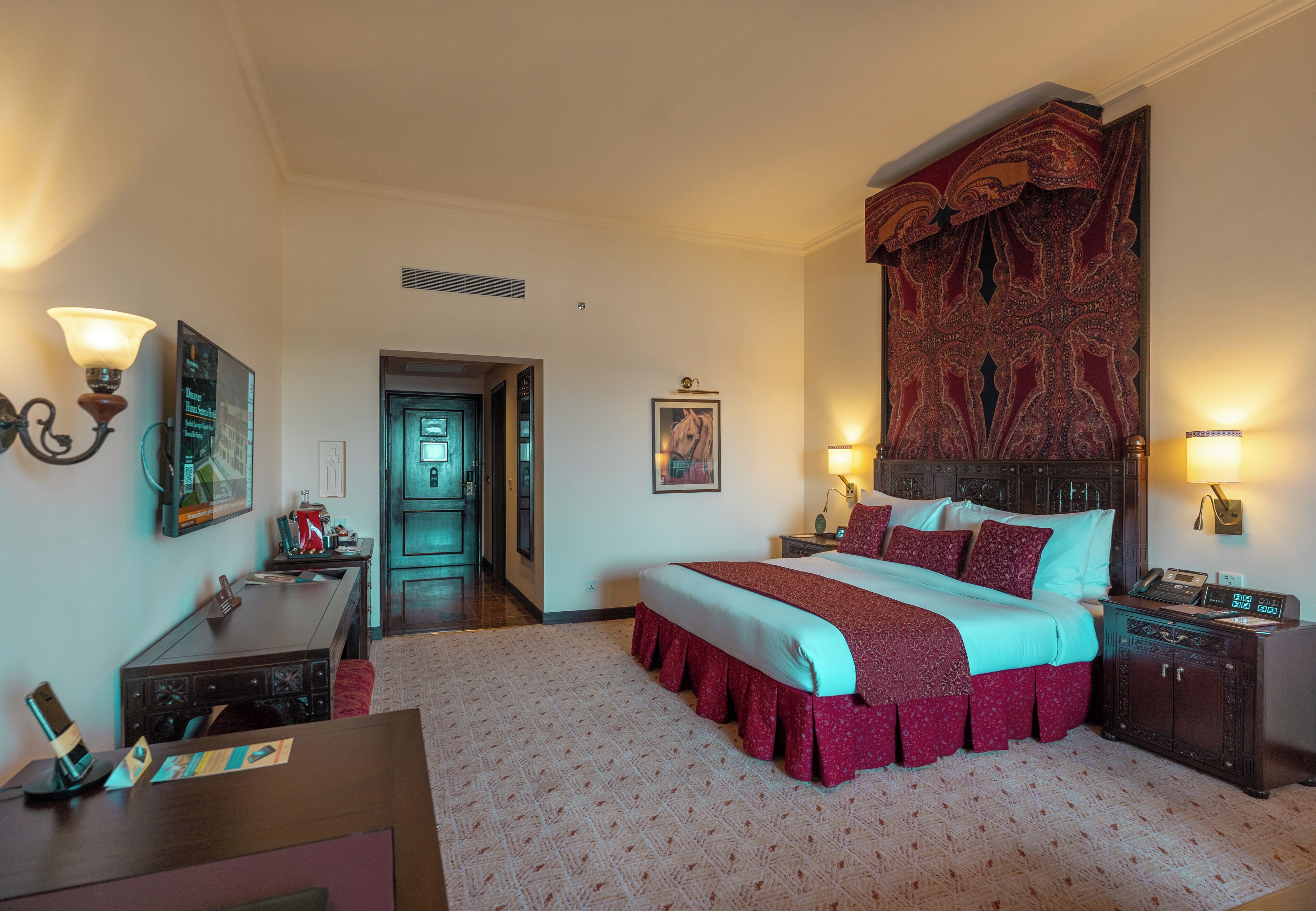 A hotel room with a large bed, a desk, a chair, a nightstand, a lamp, and a telephone.