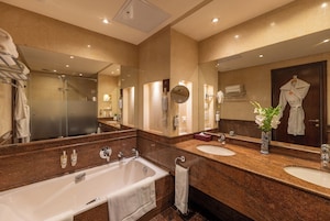 A modern bathroom with a large mirror, two sinks, a bathtub, and a shower.