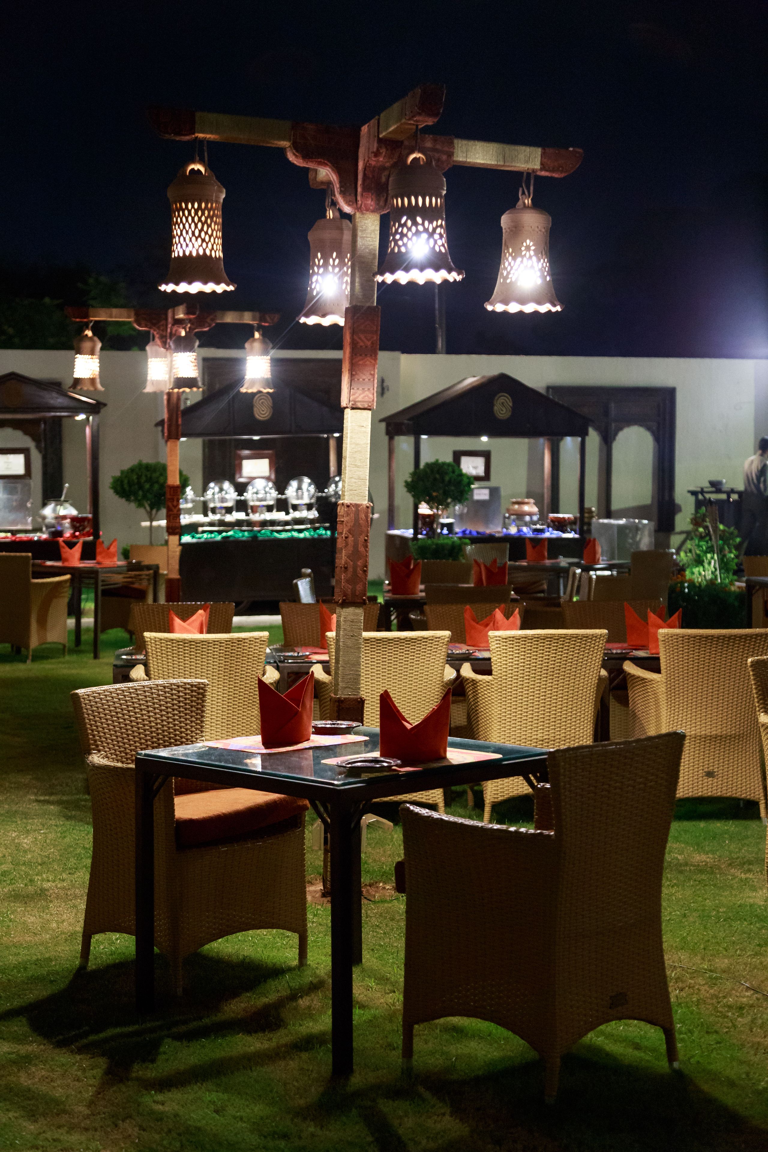 An outdoor dining area with wicker chairs and tables, illuminated by hanging lanterns.
