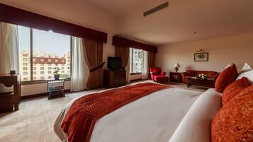 Habitación de hotel con una cama grande, televisión, escritorio y una silla. Hay una ventana con cortinas y vistas a edificios.