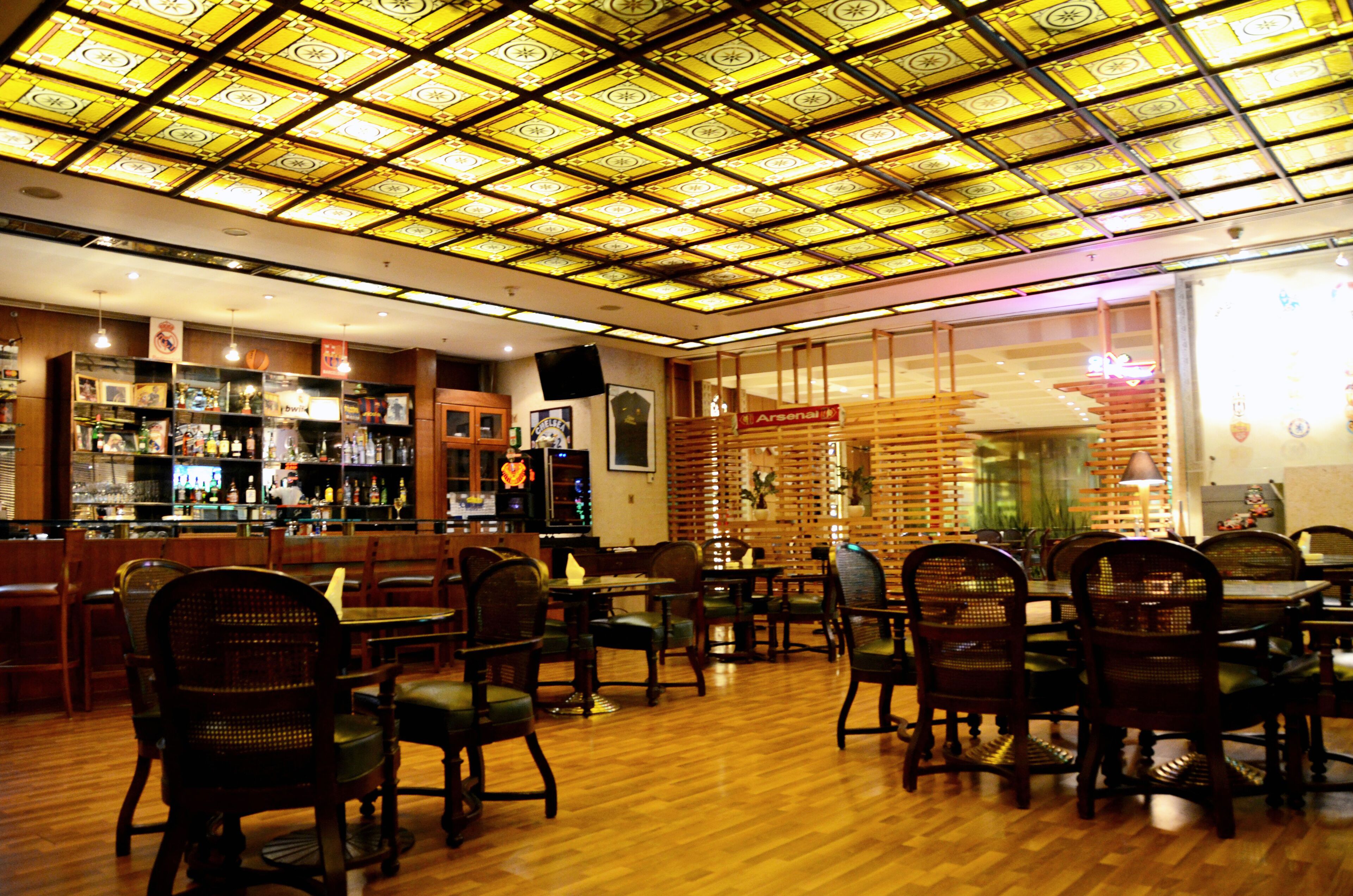 A restaurant with a patterned ceiling, wooden furniture, and a bar area.