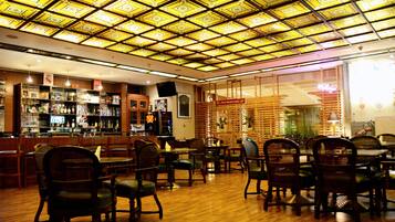 A restaurant with a patterned ceiling, wooden furniture, and a bar area.