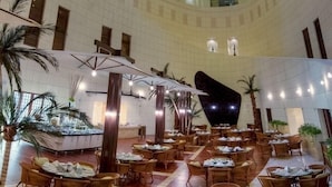 A spacious lobby with multiple dining areas, a central water feature, and a high ceiling with skylights. - Le Royal Hotel Amman (Amman)