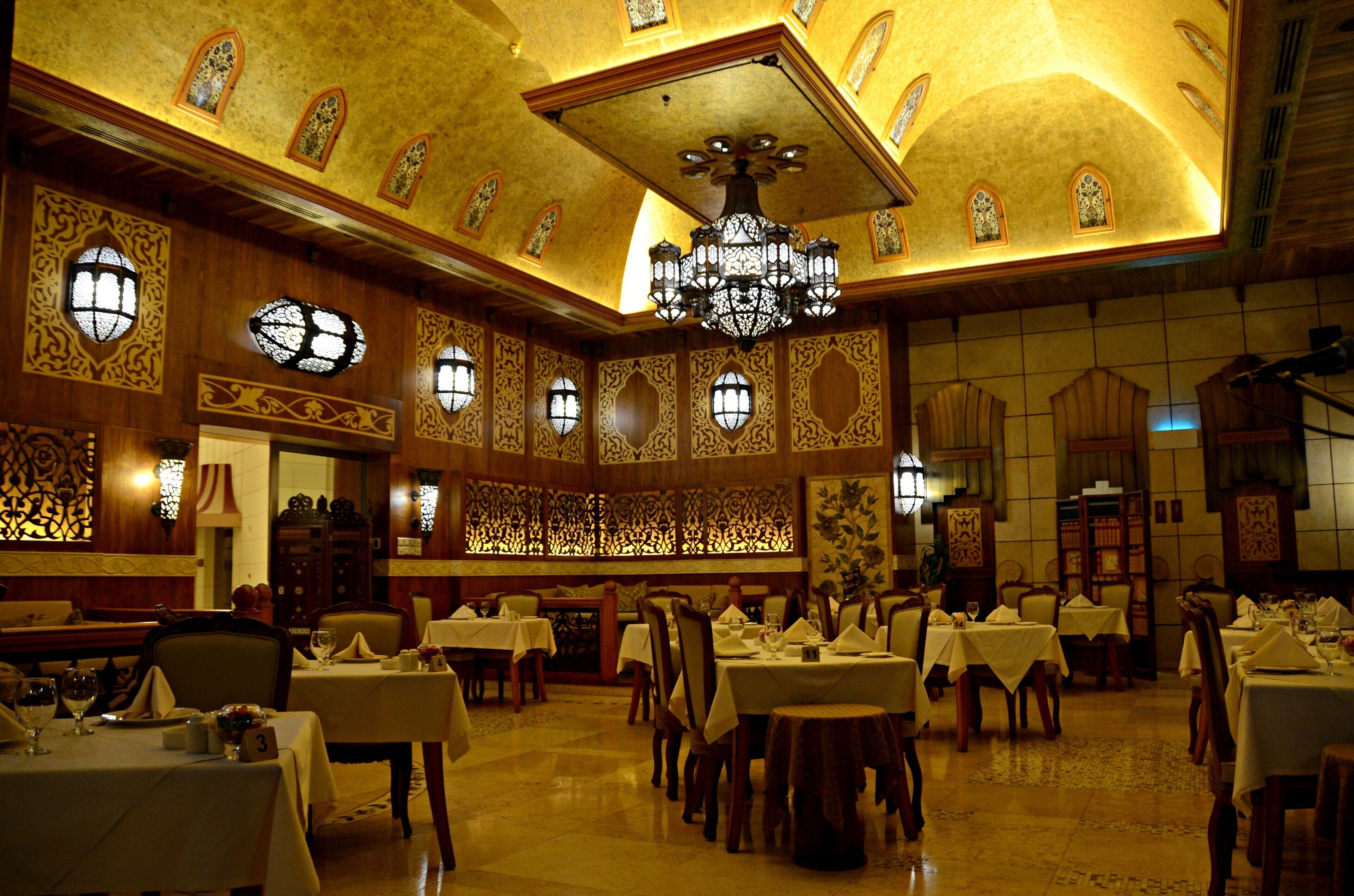 A dining area with multiple tables and chairs, ornate ceiling, and decorative windows.