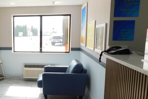 A hotel reception area with a blue sofa, a large window with a view of the street, and a reception desk with a phone. - Days Inn by Wyndham Effingham (Effingham)