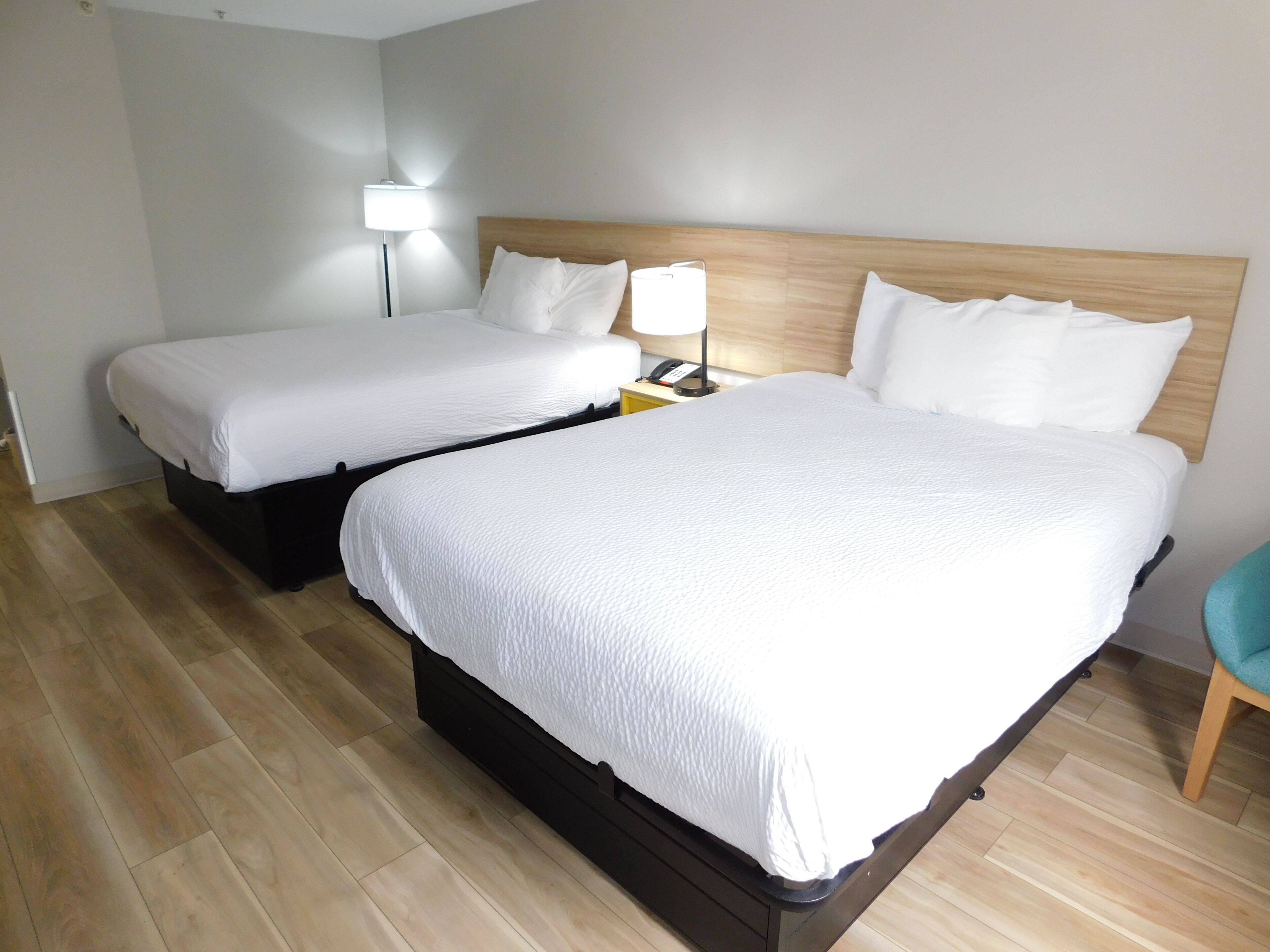 Quarto de hotel com duas camas, uma mesa de cabeceira com abajur e uma cadeira.