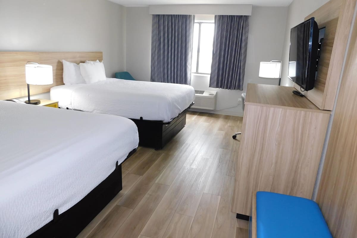 A hotel room with two beds, a TV, a desk, and a chair.