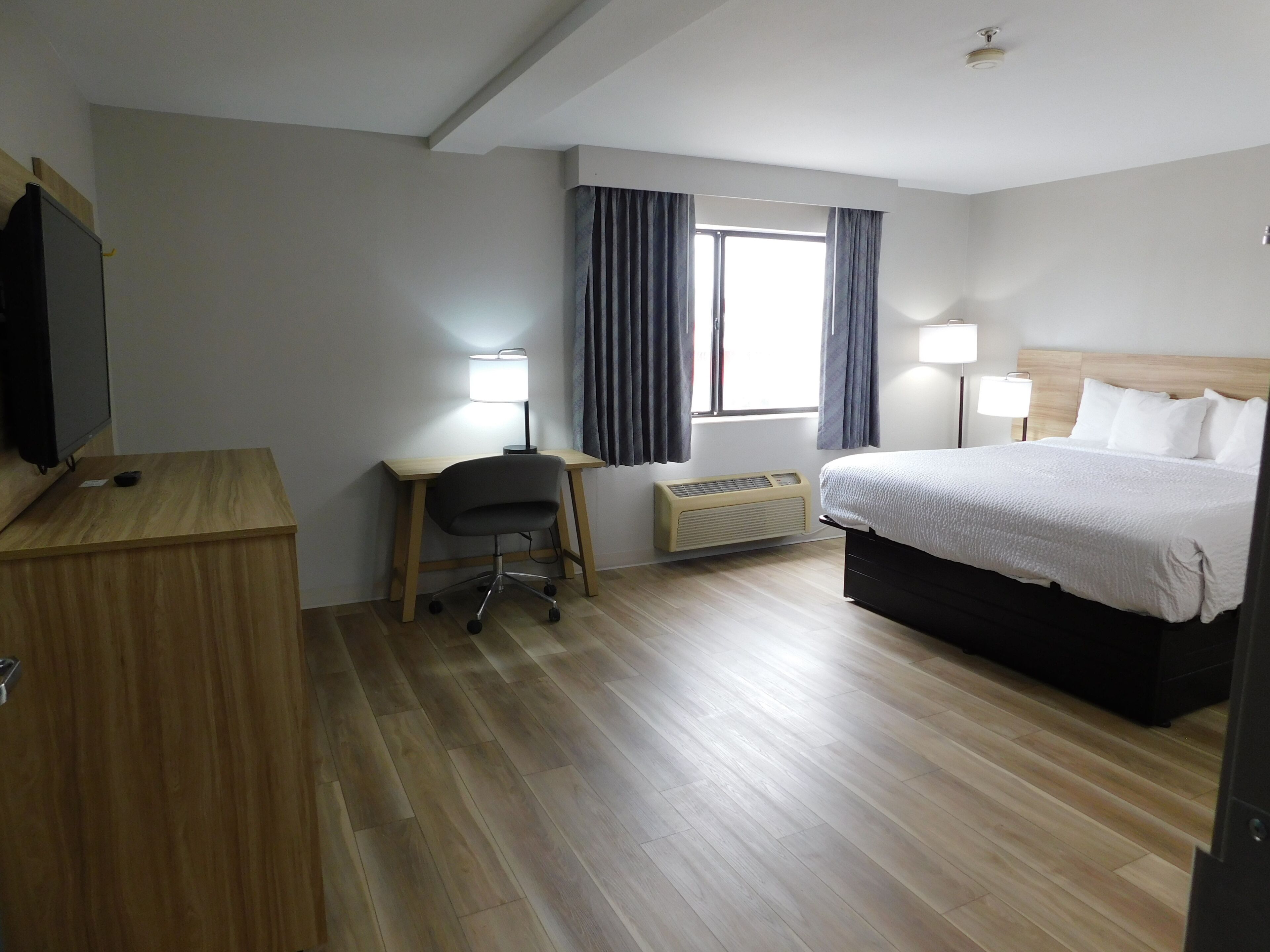 Ein Hotelzimmer mit Bett, Schreibtisch, Stuhl, Fernseher und zwei Nachttischlampen.