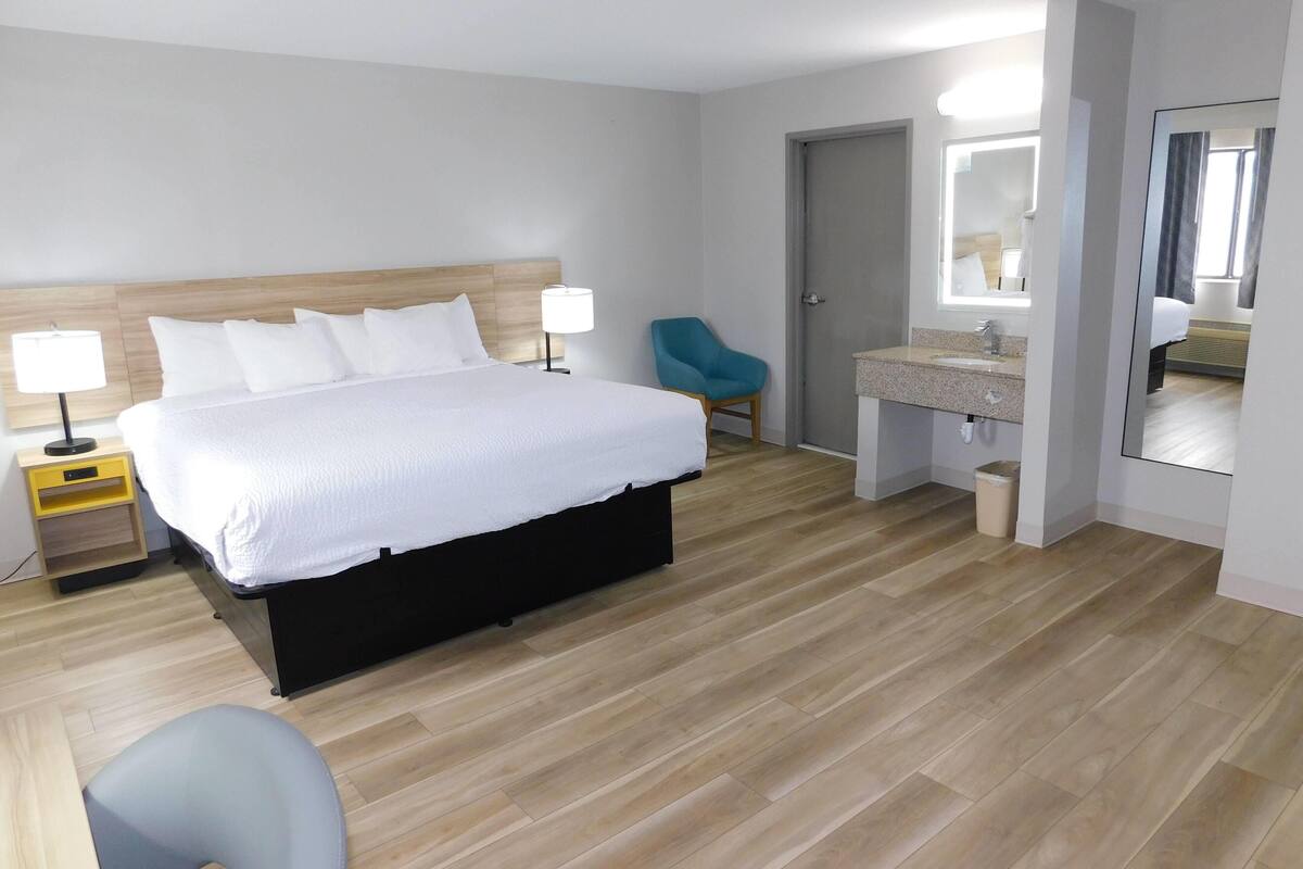 A hotel room with a bed, bedside table, chair, and a bathroom with a mirror and sink.