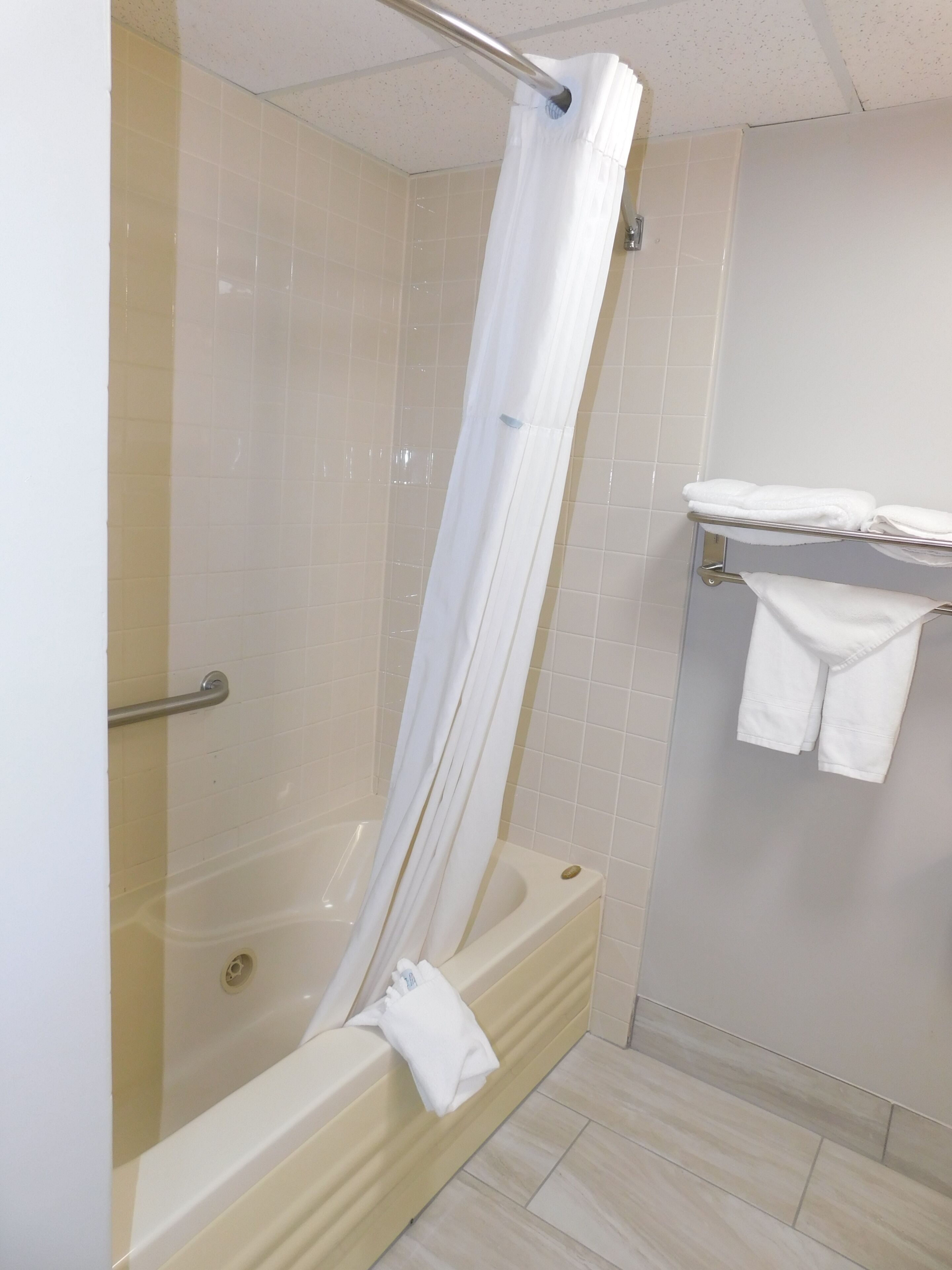 Un baño con ducha envuelta en vidrio, una bañera y un perchero con toallas dobladas.