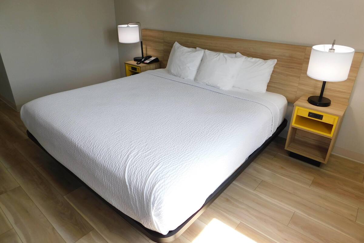 A neatly made bed with a white comforter, two bedside lamps, and a wooden headboard.