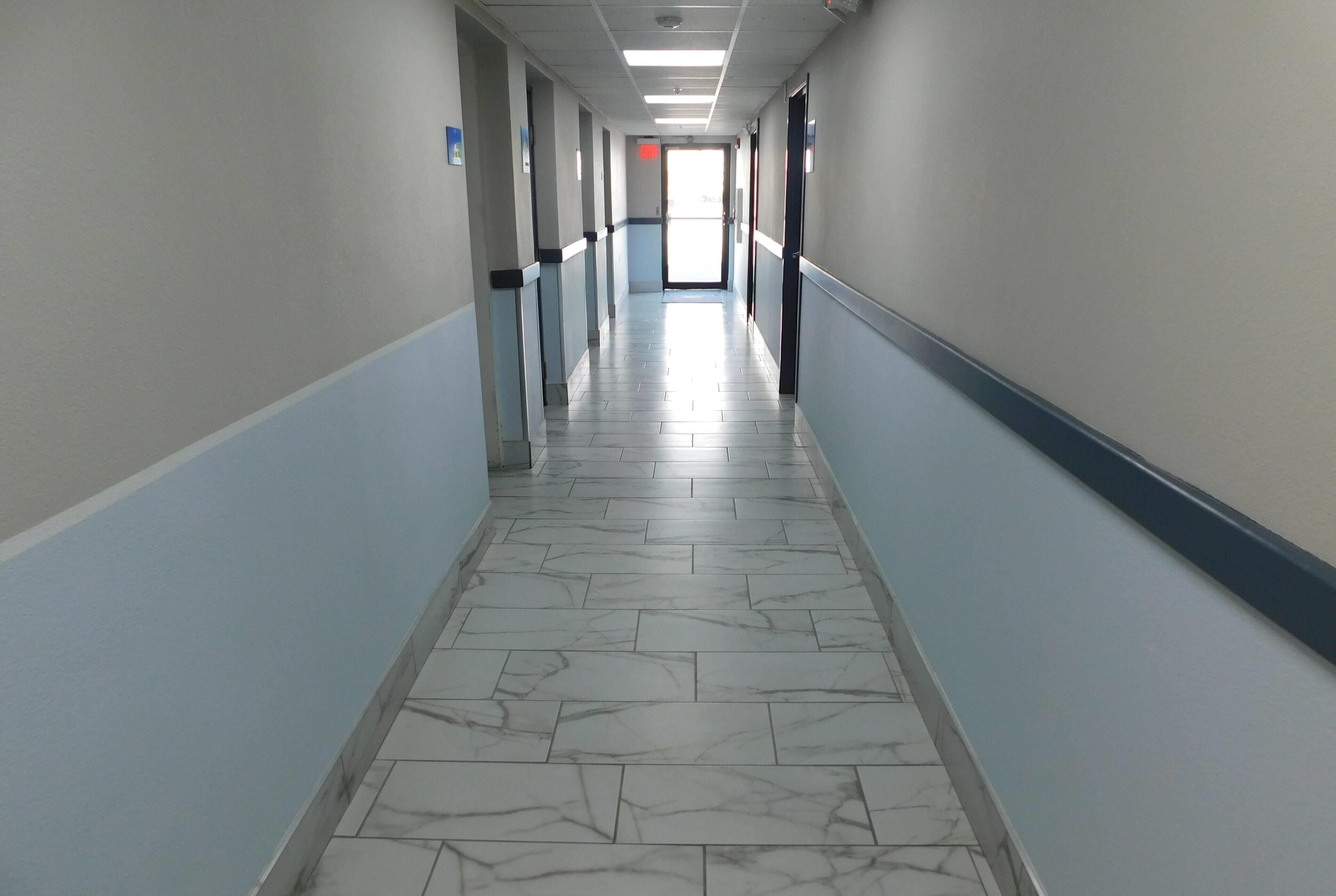 A long, narrow hallway with marble-patterned flooring and light blue walls.