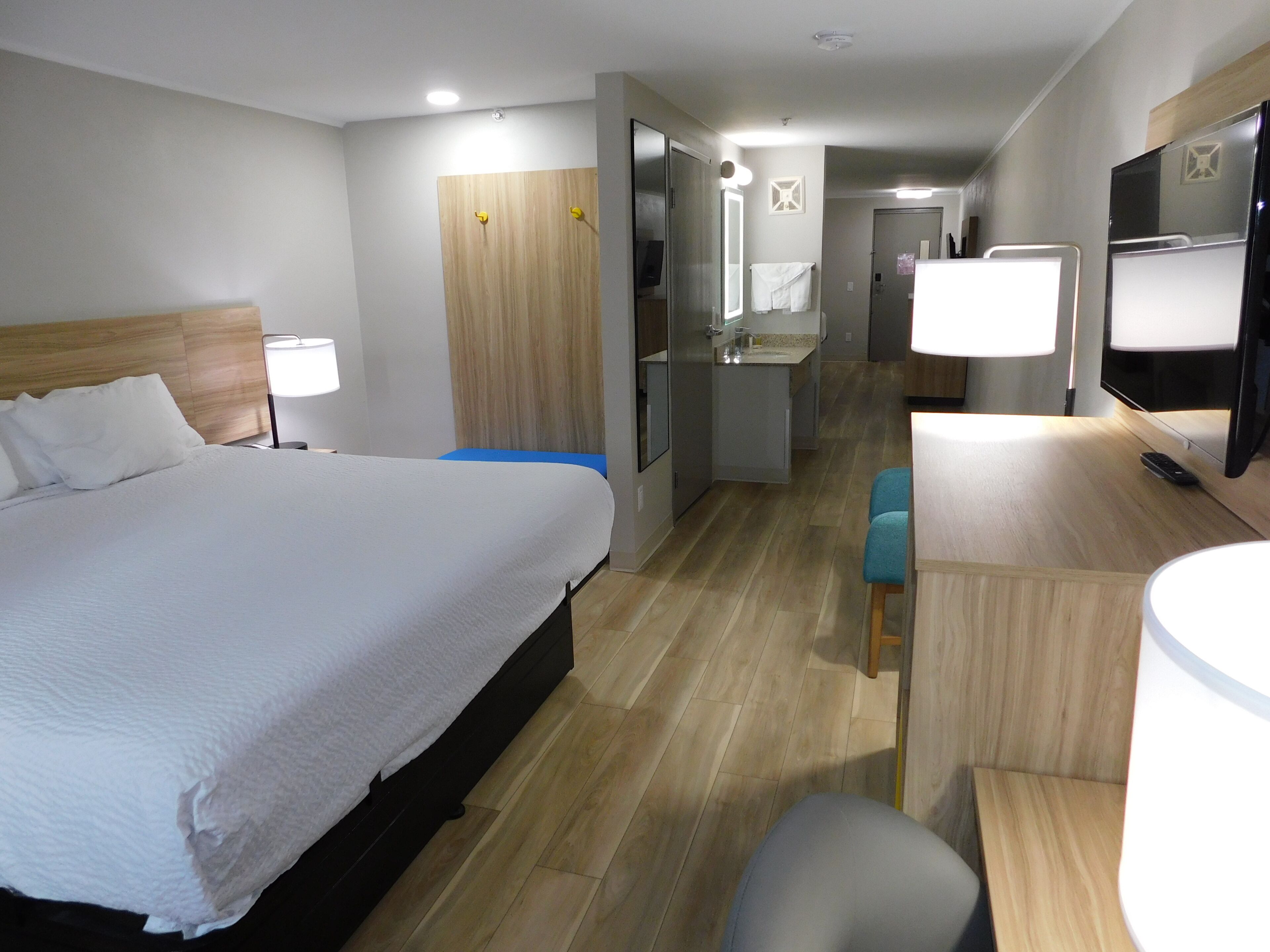 A hotel room with a bed, a desk, a chair, a mirror, a TV, and a bathroom.