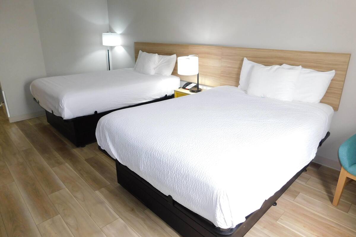 A hotel room with two beds, a nightstand with a lamp, and a wooden floor.