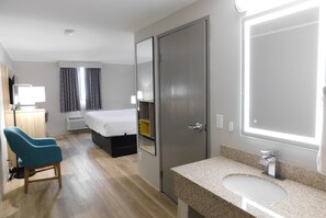 A hotel room with a bed, a desk, a chair, a bathroom with a sink and mirror, and a door. - Days Inn by Wyndham Effingham (Effingham)