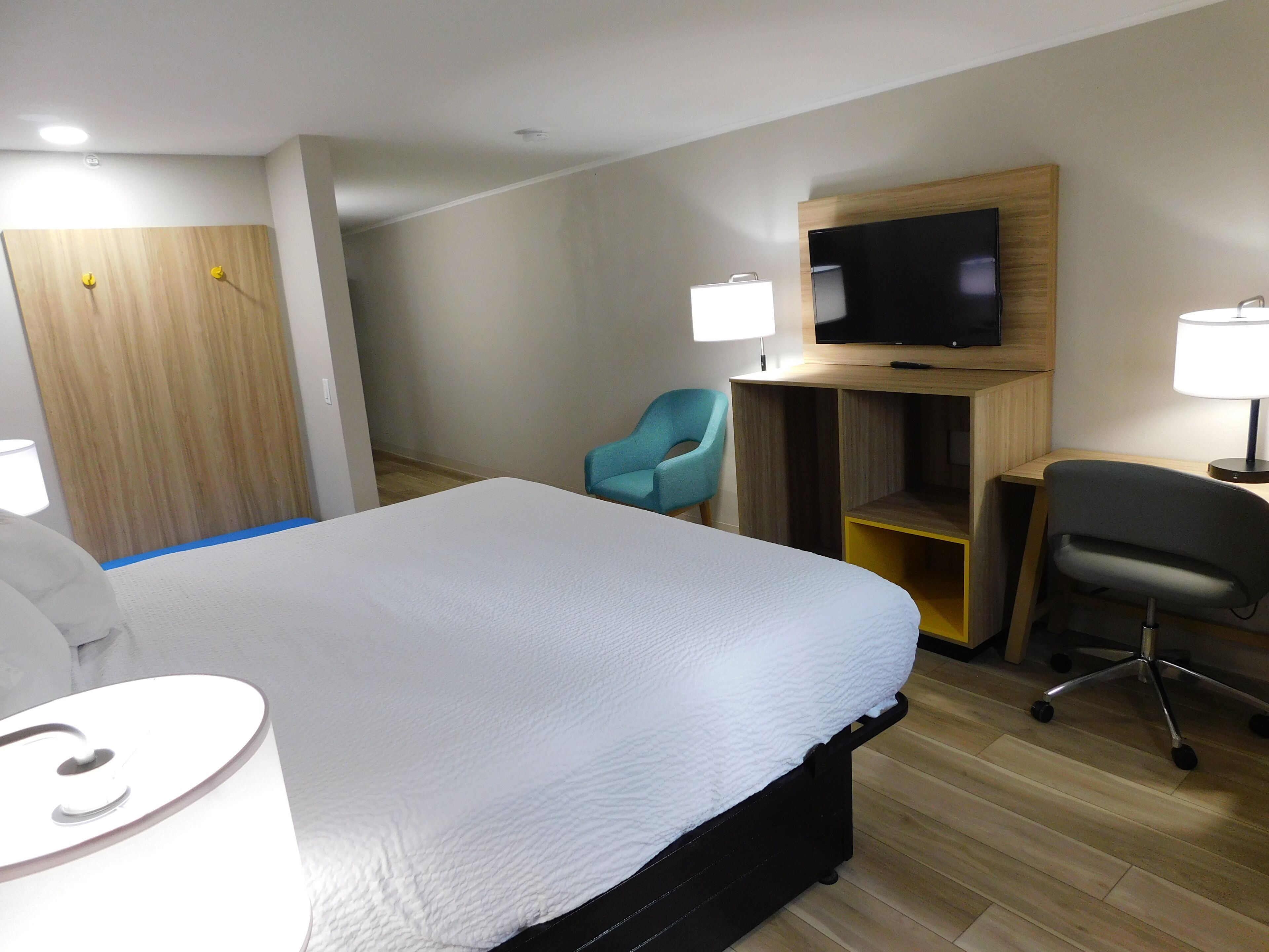 Ett hotellrum med en säng, en tv, ett skrivbord med en stol och en lampa.