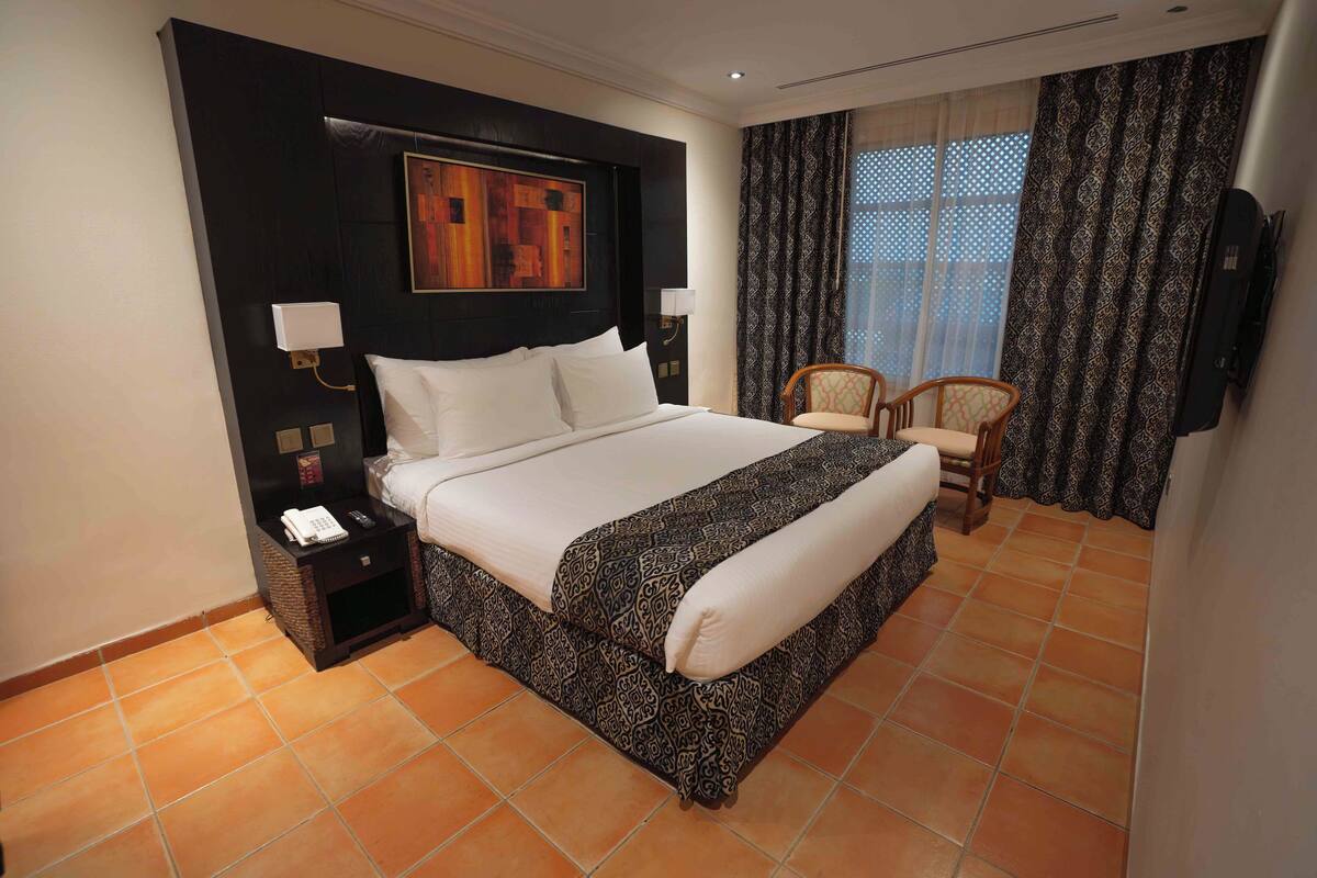 A hotel room with a large bed, a nightstand with a phone, a chair, and a TV mounted on the wall.