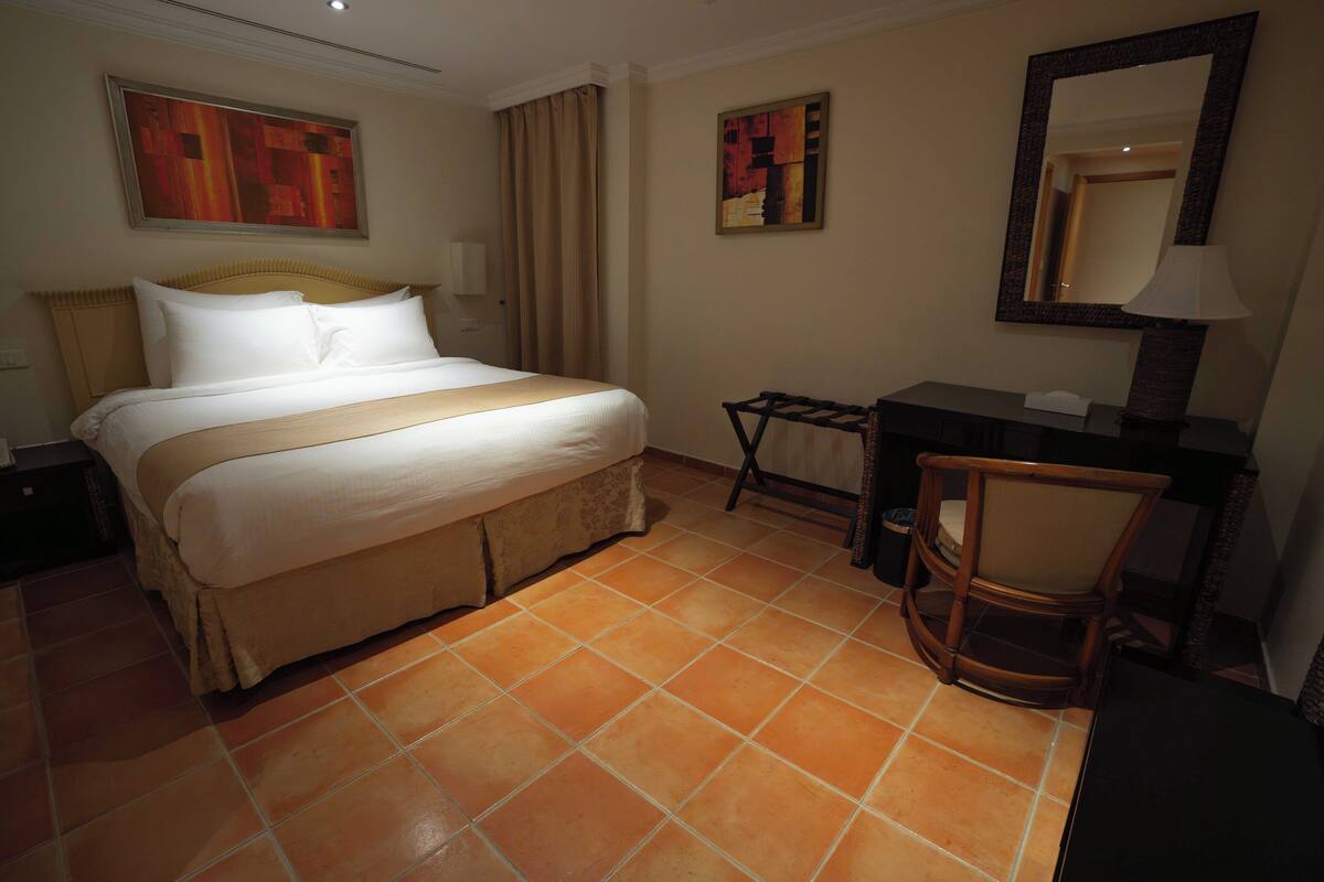 A hotel room with a bed, a desk, a chair, and a large mirror.