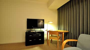 A hotel room with a flat-screen TV on a black stand, a wooden chair, a small round table, and a lamp.