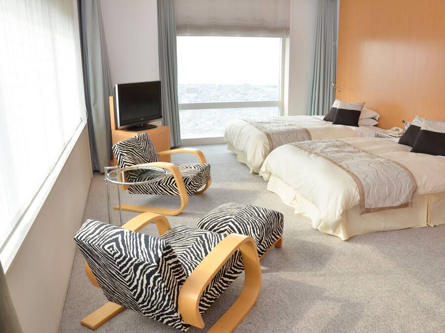 Een hotelkamer met twee bedden, een televisie, een stoel en uitzicht op de stad.