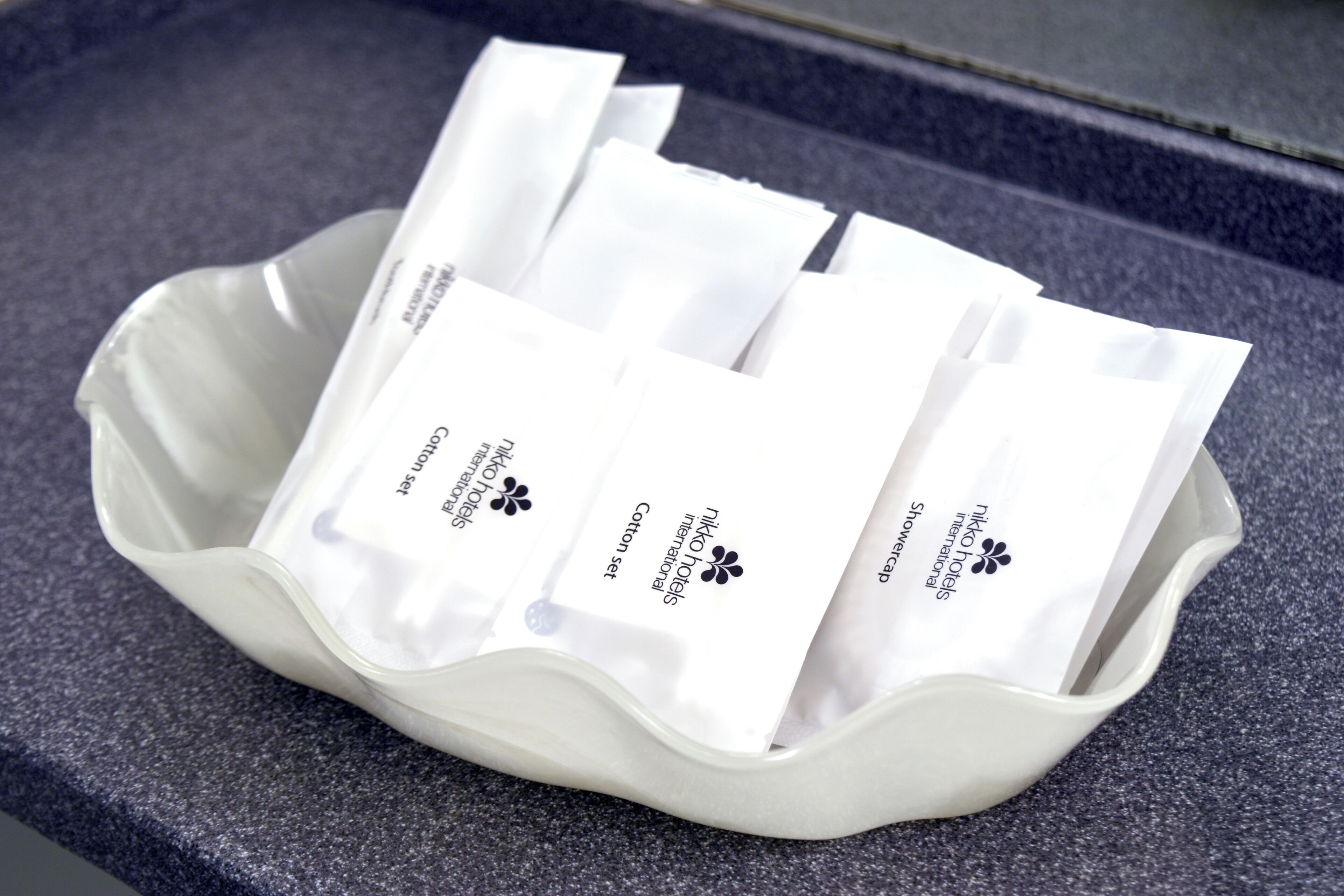 A white tray containing several white packets labeled "nikko hotels international cotton set shower cap."
