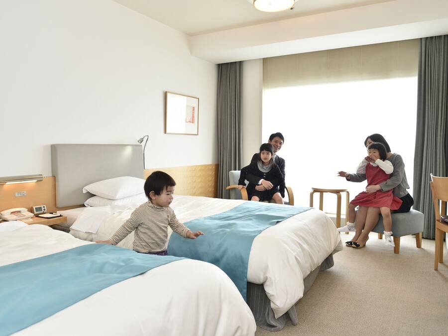 A hotel room with two beds, a desk, a chair, and a bedside table with a lamp and phone.