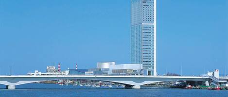 A modern high-rise building with a glass facade, a bridge spanning a body of water, and a boat in the foreground.