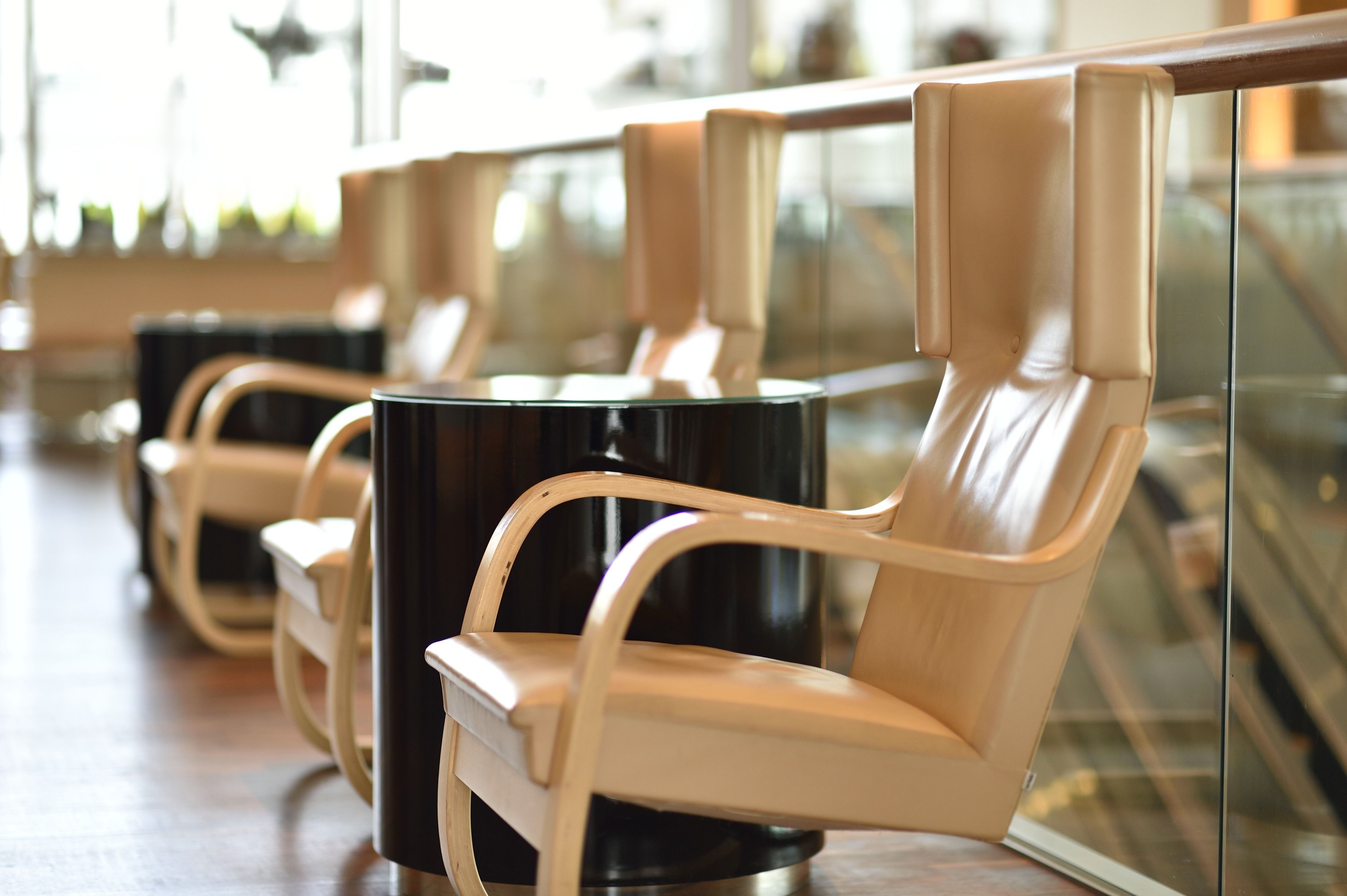 A row of modern, beige upholstered chairs with black bases, arranged in a public space with a glass partition in the background.