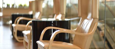 Une rangée de chaises modernes, de couleur beige, avec un revêtement en tissu et des pieds noirs, disposées dans un espace public, avec une cloison en verre en arrière-plan.